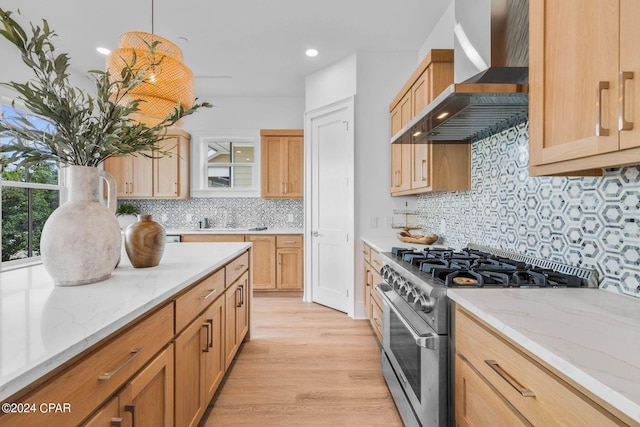 kitchen with hanging light fixtures, tasteful backsplash, high end stainless steel range oven, light hardwood / wood-style flooring, and wall chimney range hood