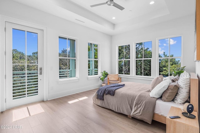 bedroom with light wood-type flooring, access to outside, ceiling fan, and a raised ceiling