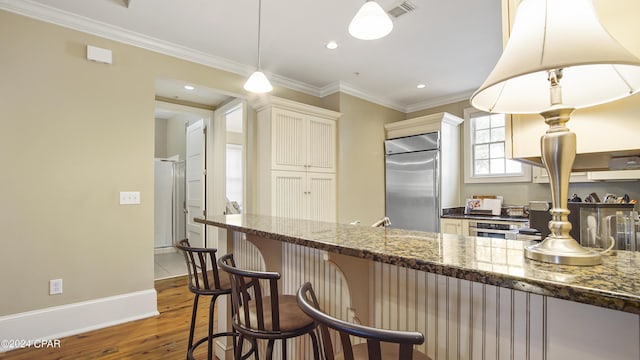 kitchen featuring a breakfast bar area, wood finished floors, built in fridge, visible vents, and ornamental molding