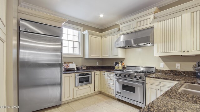 kitchen with cream cabinetry, premium appliances, dark stone counters, ornamental molding, and sink