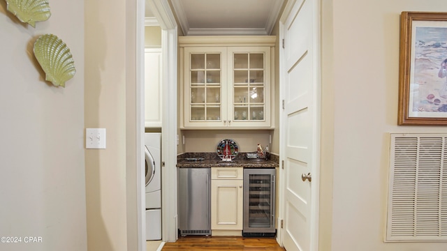 bar featuring cream cabinetry, light hardwood / wood-style floors, beverage cooler, dark stone counters, and ornamental molding