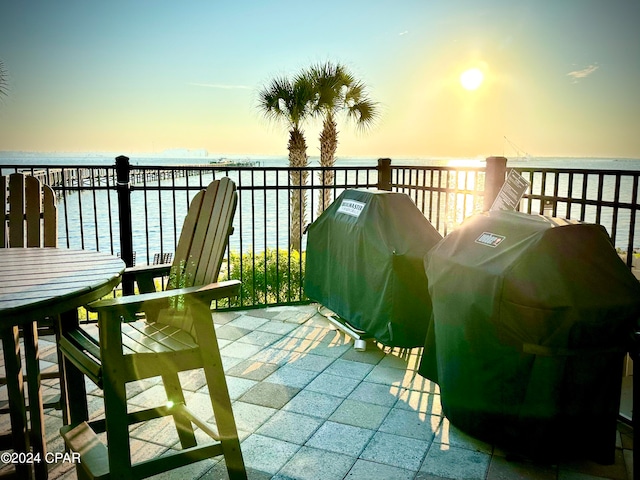 balcony at dusk featuring grilling area and a water view