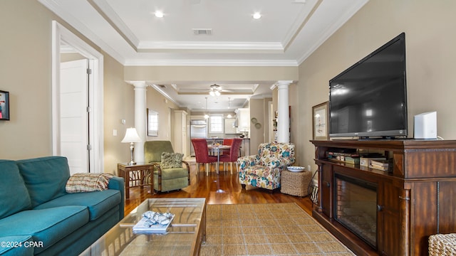 living room featuring crown molding, a tray ceiling, ceiling fan, decorative columns, and dark hardwood / wood-style floors