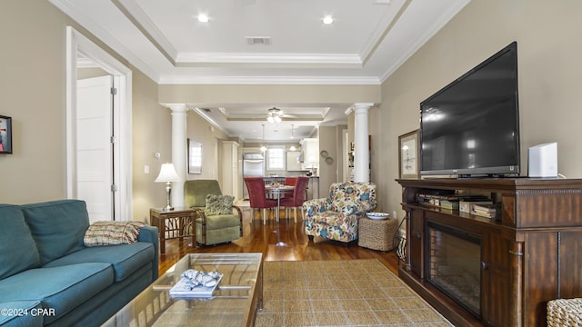 living room with a tray ceiling, visible vents, decorative columns, and wood finished floors