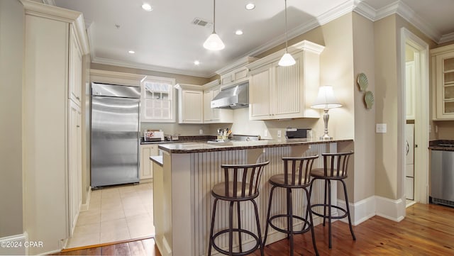 kitchen featuring pendant lighting, stainless steel appliances, a kitchen bar, and light hardwood / wood-style flooring