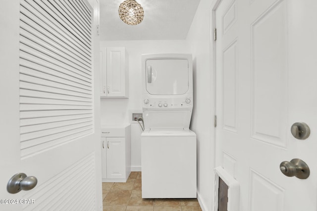 laundry room with stacked washer and clothes dryer, cabinets, and a textured ceiling