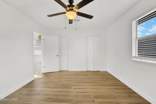 unfurnished bedroom with light wood-type flooring, multiple closets, and ceiling fan