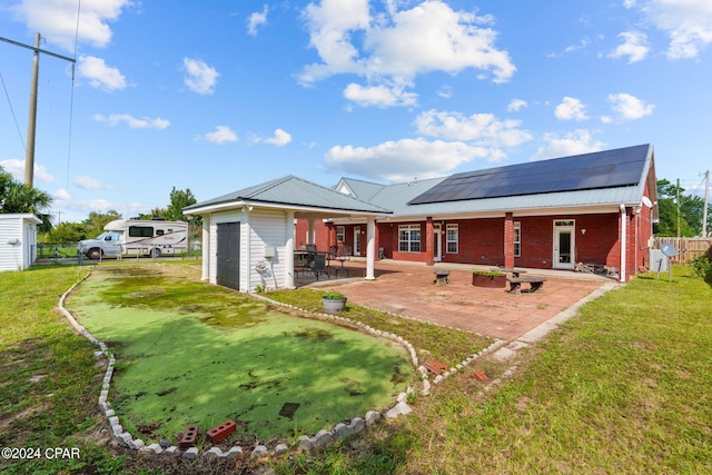 rear view of house with solar panels, a lawn, a patio area, and an outbuilding