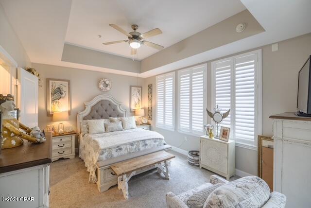 bedroom featuring light colored carpet, ceiling fan, and a tray ceiling