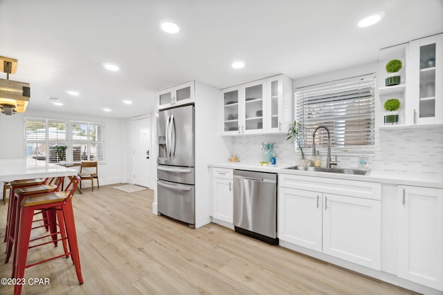 kitchen with white cabinets, sink, appliances with stainless steel finishes, light hardwood / wood-style floors, and decorative backsplash