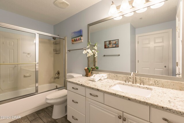 full bathroom with wood-type flooring, a textured ceiling, vanity, enclosed tub / shower combo, and toilet