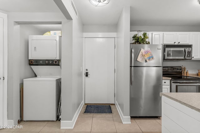 kitchen with appliances with stainless steel finishes, white cabinetry, light tile patterned floors, and stacked washer / dryer