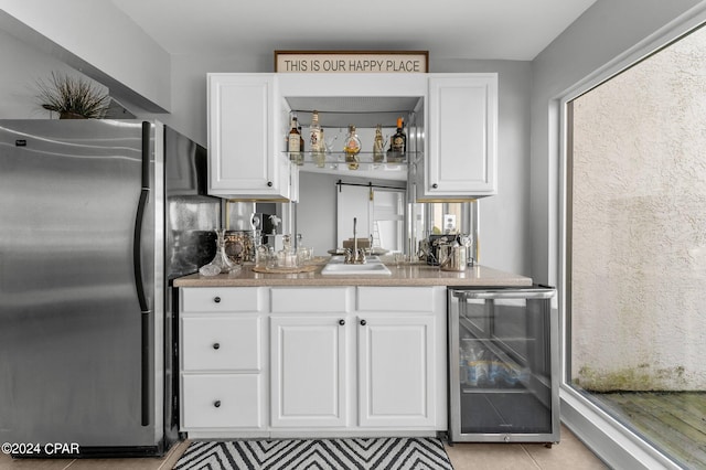 interior space featuring sink, beverage cooler, white cabinetry, stainless steel refrigerator, and light tile patterned floors