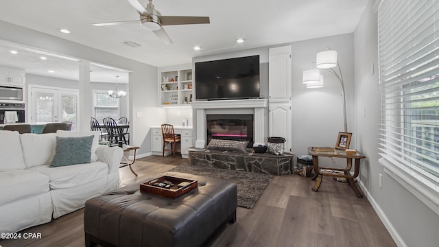 living room with ceiling fan with notable chandelier, dark wood-type flooring, and a wealth of natural light