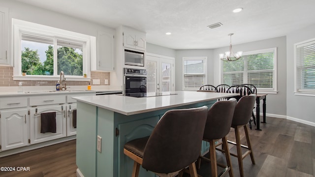 kitchen featuring hanging light fixtures, black appliances, a kitchen island, and white cabinetry