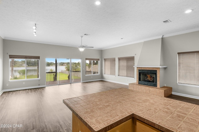 kitchen featuring ceiling fan, a tiled fireplace, dark wood-type flooring, and a healthy amount of sunlight