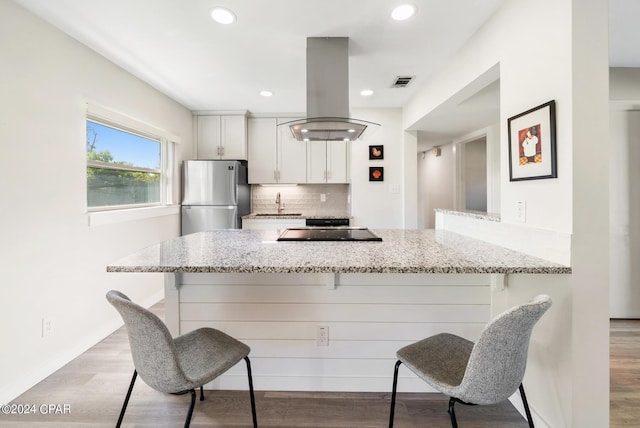 kitchen with stainless steel refrigerator, white cabinetry, kitchen peninsula, a breakfast bar area, and island range hood