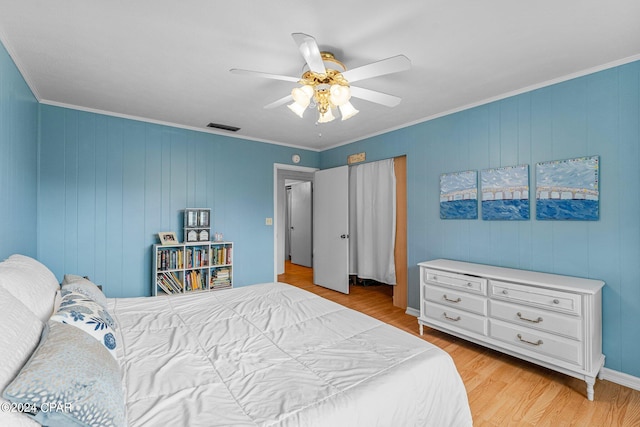 bedroom with ceiling fan, light wood-type flooring, crown molding, and wood walls