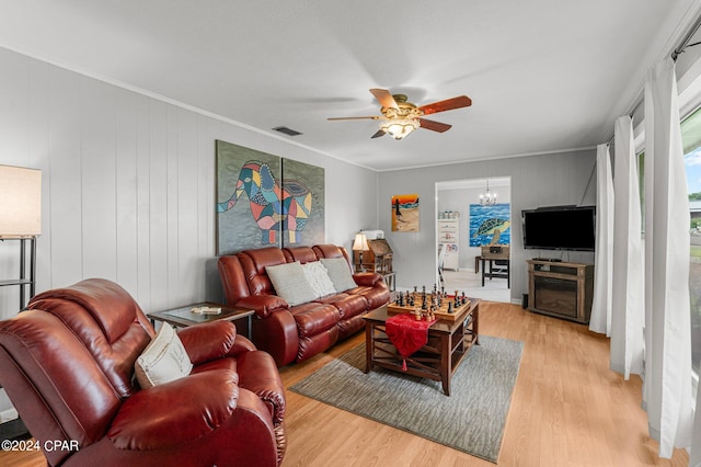 living room with ceiling fan with notable chandelier, light wood-type flooring, crown molding, and wood walls