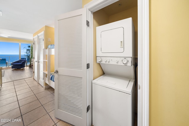 laundry room with stacked washer and clothes dryer, light tile patterned flooring, and a water view