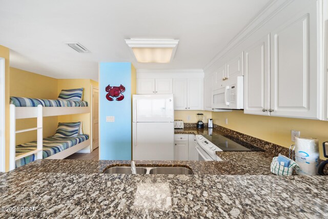 kitchen with dark stone counters, sink, white cabinets, white appliances, and ornamental molding