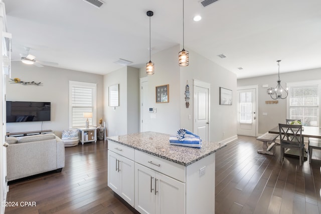 kitchen featuring white cabinets, light stone countertops, hanging light fixtures, dark wood-type flooring, and ceiling fan with notable chandelier