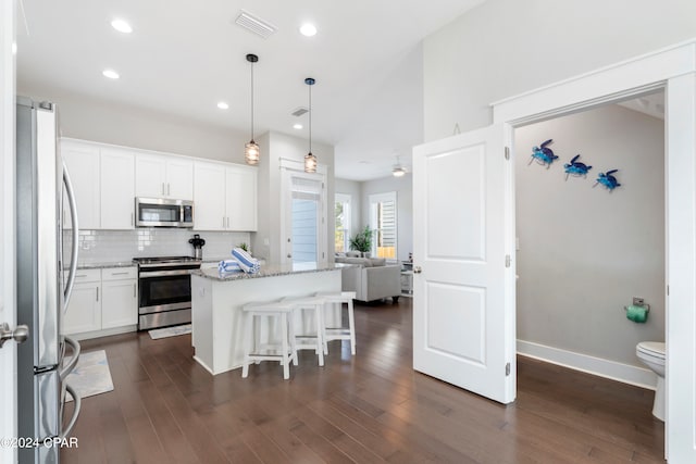 kitchen with light stone counters, a kitchen island, white cabinetry, appliances with stainless steel finishes, and dark hardwood / wood-style flooring