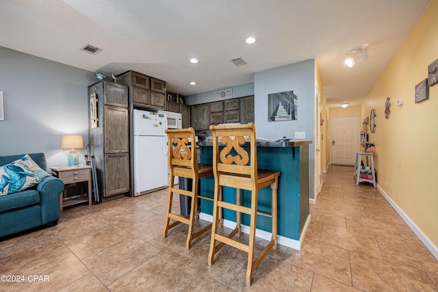 kitchen with white appliances, light tile patterned flooring, and dark brown cabinetry