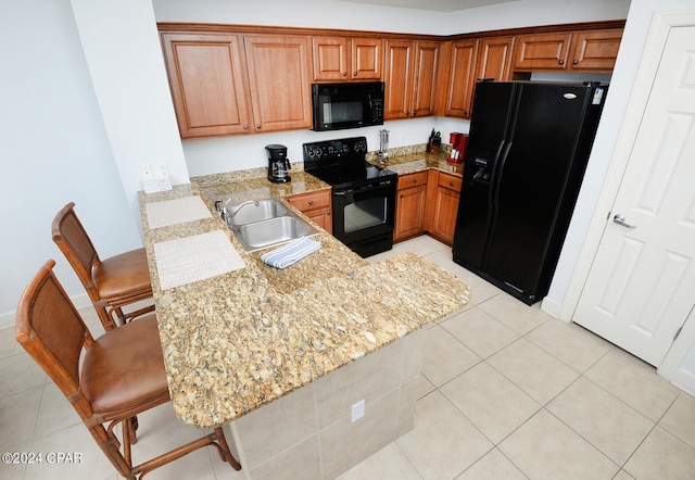 kitchen featuring light stone counters, a breakfast bar, kitchen peninsula, black appliances, and sink