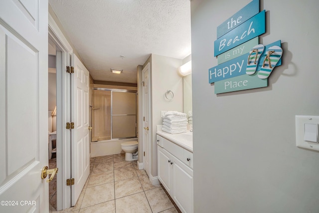 full bathroom featuring shower / bath combination with glass door, vanity, a textured ceiling, tile patterned floors, and toilet