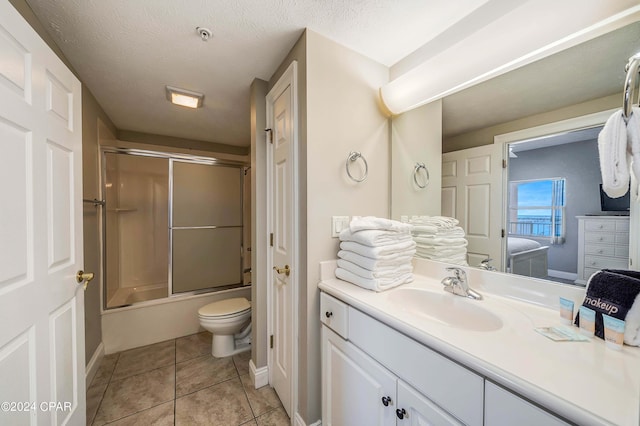 full bathroom with combined bath / shower with glass door, tile patterned flooring, vanity, toilet, and a textured ceiling