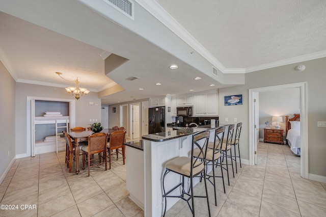 kitchen with light tile patterned flooring, white cabinetry, a kitchen bar, black appliances, and crown molding