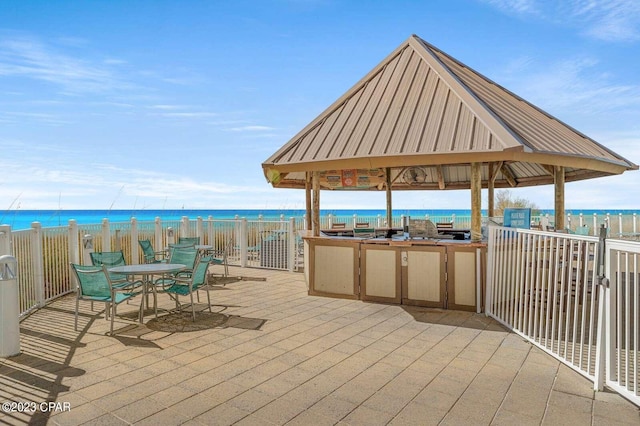 view of patio featuring a gazebo, a water view, outdoor dining space, and a view of the beach