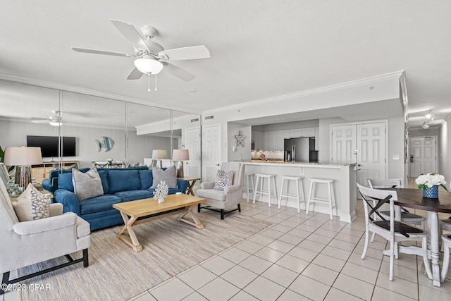 living area with a textured ceiling, ornamental molding, light tile patterned flooring, and ceiling fan