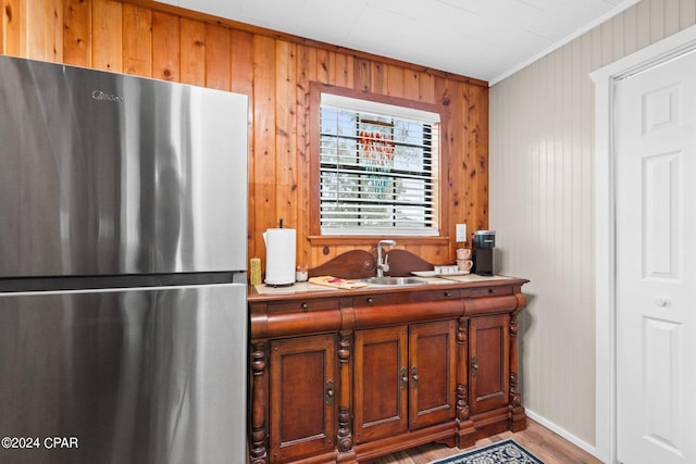 kitchen featuring stainless steel refrigerator, wood walls, crown molding, hardwood / wood-style flooring, and sink