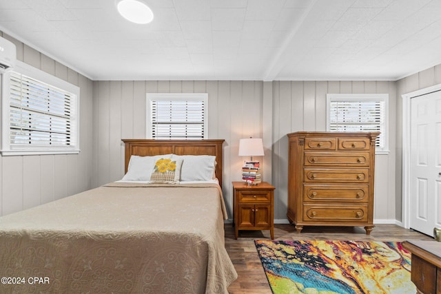 bedroom with multiple windows, wood walls, and dark wood-type flooring