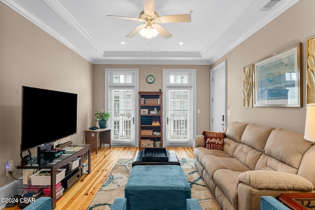 living room featuring ceiling fan, light wood-type flooring, and a tray ceiling