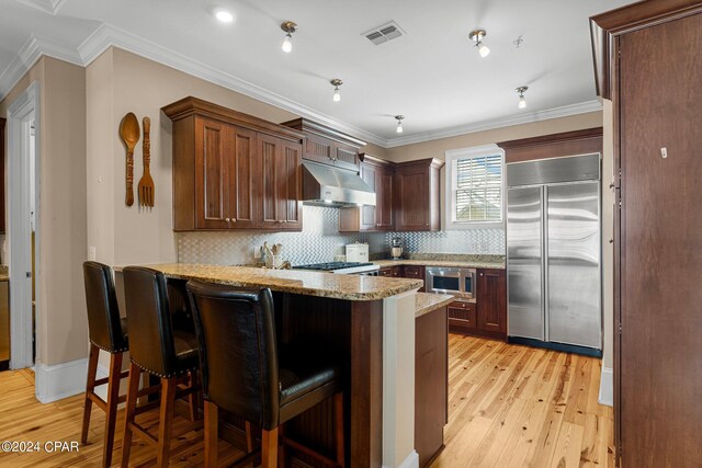 kitchen featuring ornamental molding, kitchen peninsula, built in appliances, a kitchen breakfast bar, and light wood-type flooring