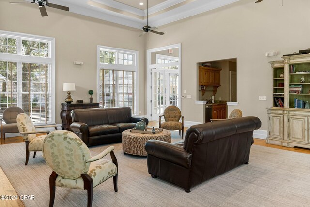 living room with ceiling fan, a raised ceiling, light hardwood / wood-style flooring, crown molding, and a towering ceiling