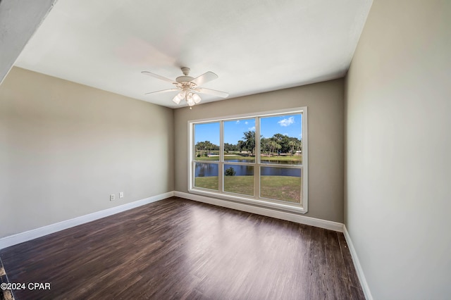 empty room with a water view, ceiling fan, and dark hardwood / wood-style flooring