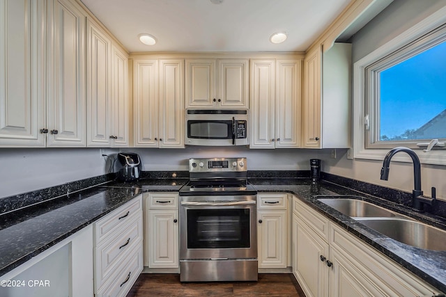 kitchen with appliances with stainless steel finishes, cream cabinetry, dark stone countertops, and sink