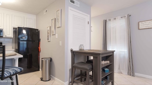 kitchen featuring light tile patterned floors, black fridge, backsplash, and white cabinets