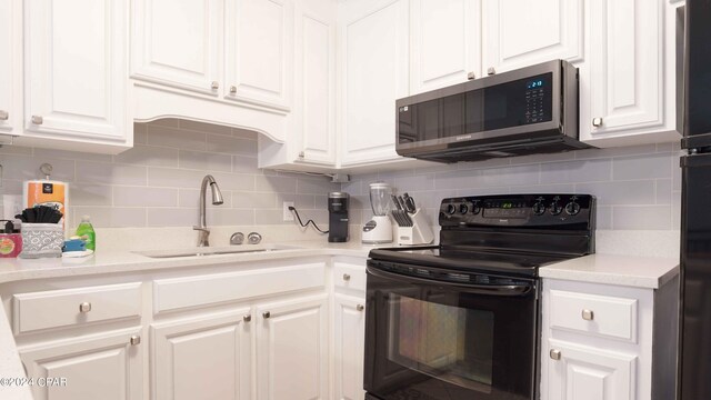 kitchen with black electric range oven, sink, and white cabinets