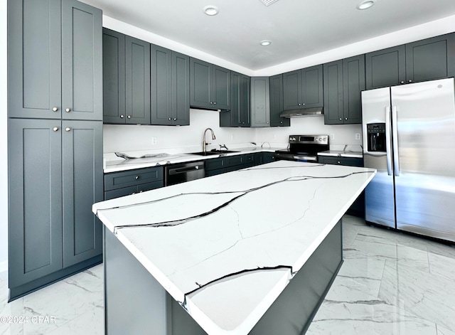 kitchen featuring appliances with stainless steel finishes, gray cabinetry, a kitchen island, light stone countertops, and sink