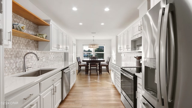 kitchen with appliances with stainless steel finishes, light hardwood / wood-style floors, white cabinetry, decorative light fixtures, and sink