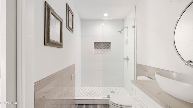 bathroom featuring wood-type flooring, tiled shower, vanity, and toilet