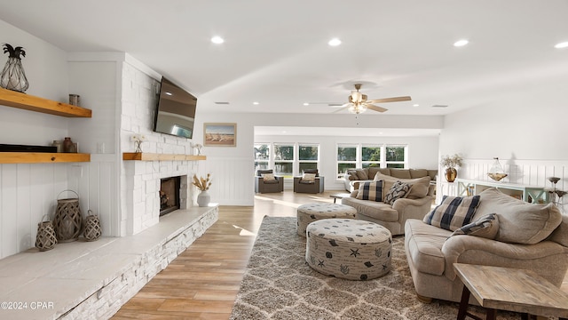 living room featuring ceiling fan, a stone fireplace, and light wood-type flooring