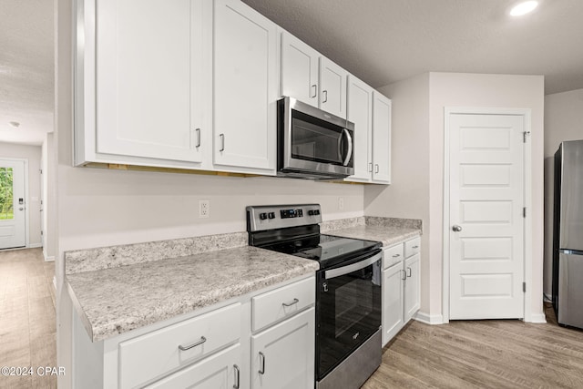 kitchen featuring appliances with stainless steel finishes, light wood-type flooring, a textured ceiling, and white cabinetry