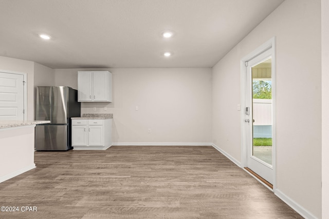 kitchen featuring light wood-type flooring, stainless steel refrigerator, white cabinetry, and light stone counters