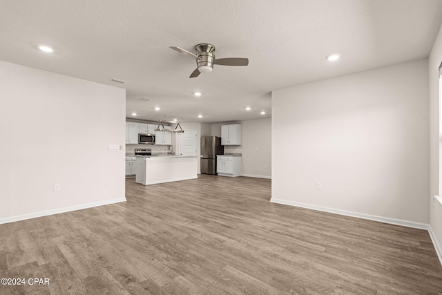 unfurnished living room featuring ceiling fan, a textured ceiling, light hardwood / wood-style flooring, and sink